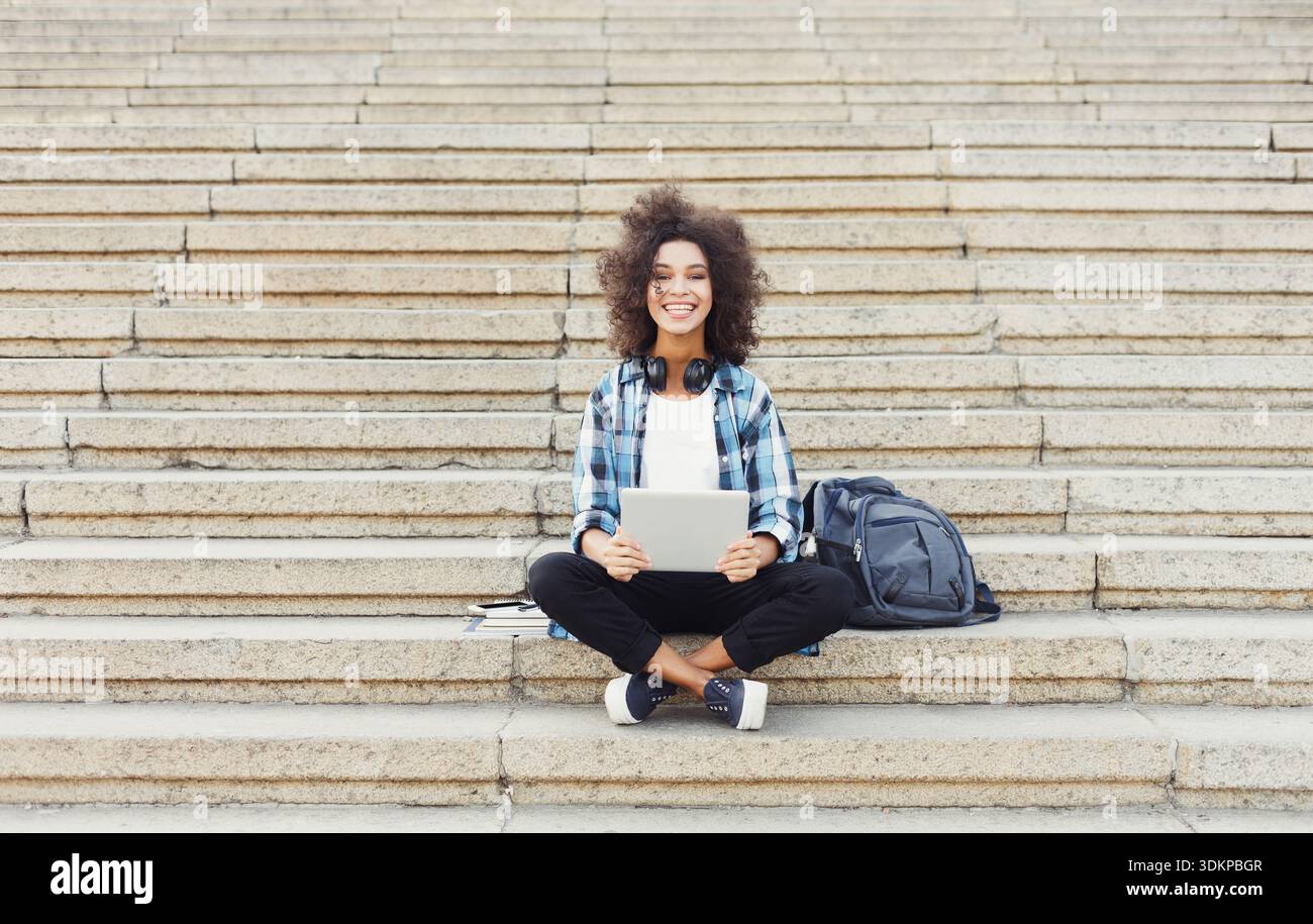 Smiling student sitting on stairs using laptop Stock Photo