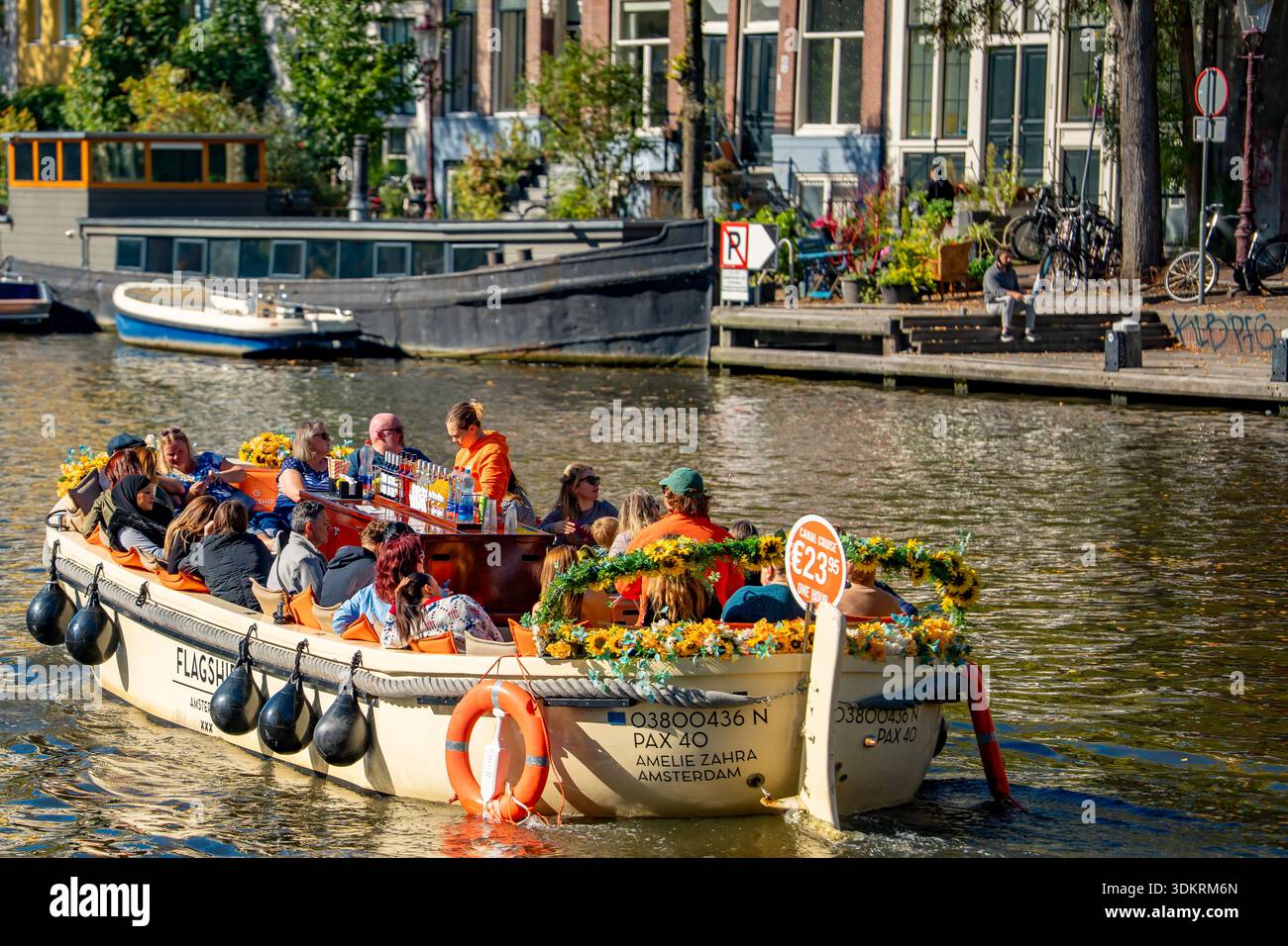 An open canal boat carrying tourists on guided tours of the canals of Amsterdam in the Netherlands Stock Photo
