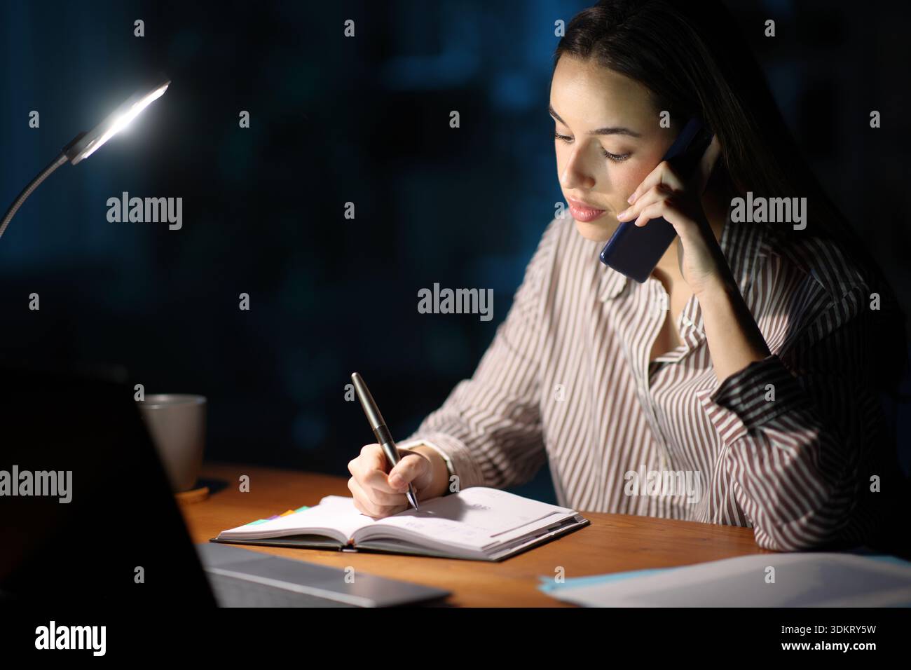 Self employed scheduling in agenda talking on phone working in the night Stock Photo