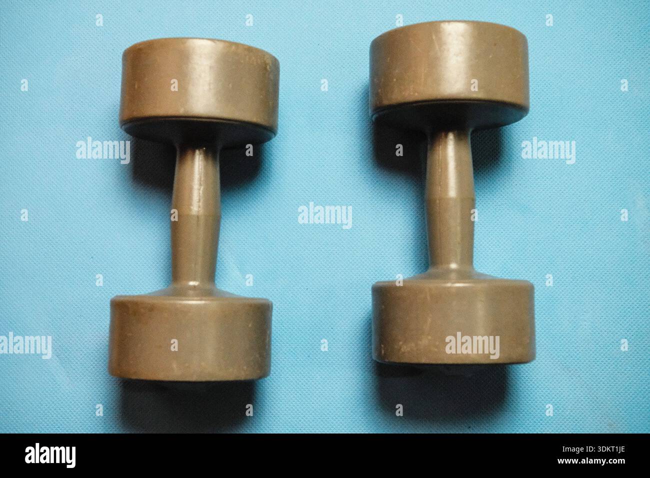 Training dumbbells resting on a light blue yoga mat Stock Photo