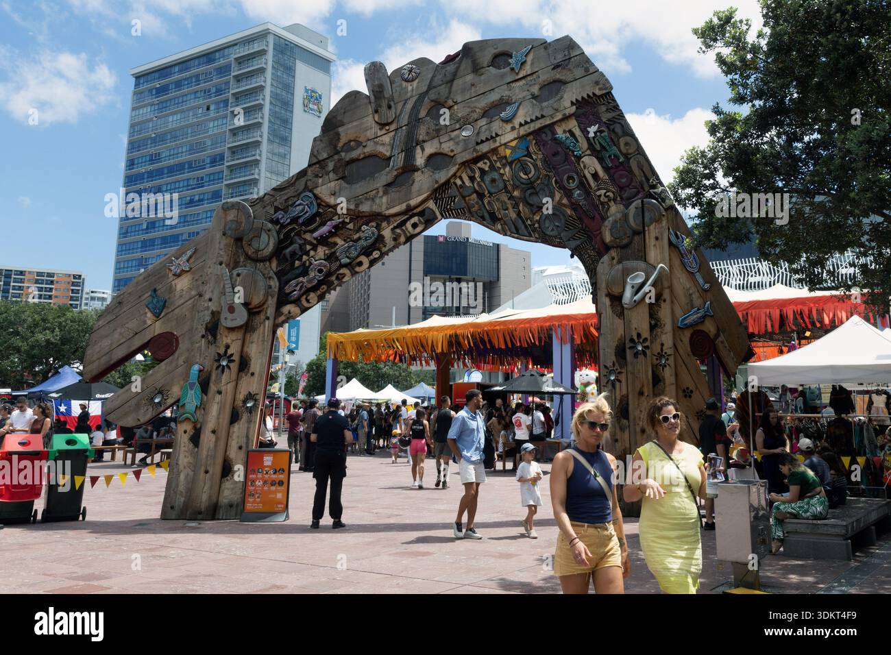 People walking beneath a large wooden archway sculpture at an outdoor market and event space in central Auckland, New Zealand. Stock Photo