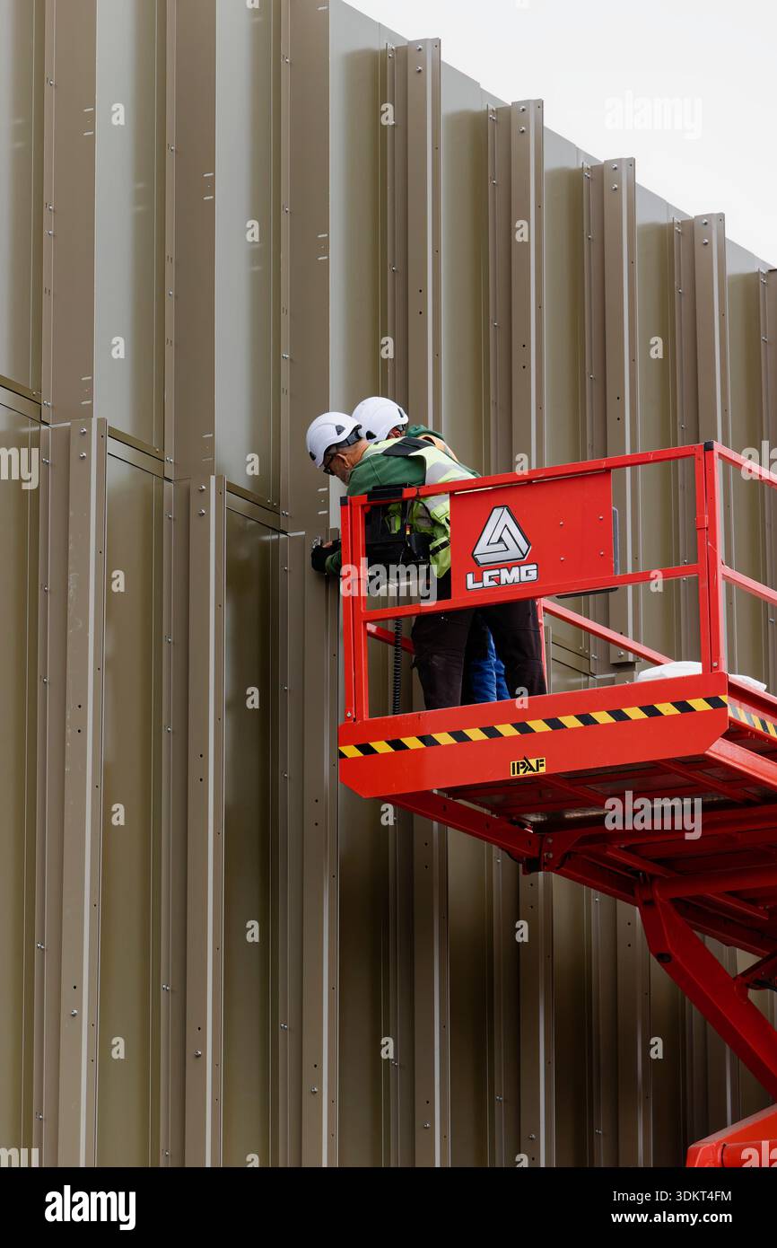 Two contractors on scissor lift fitting aluminium fins to vertical ...