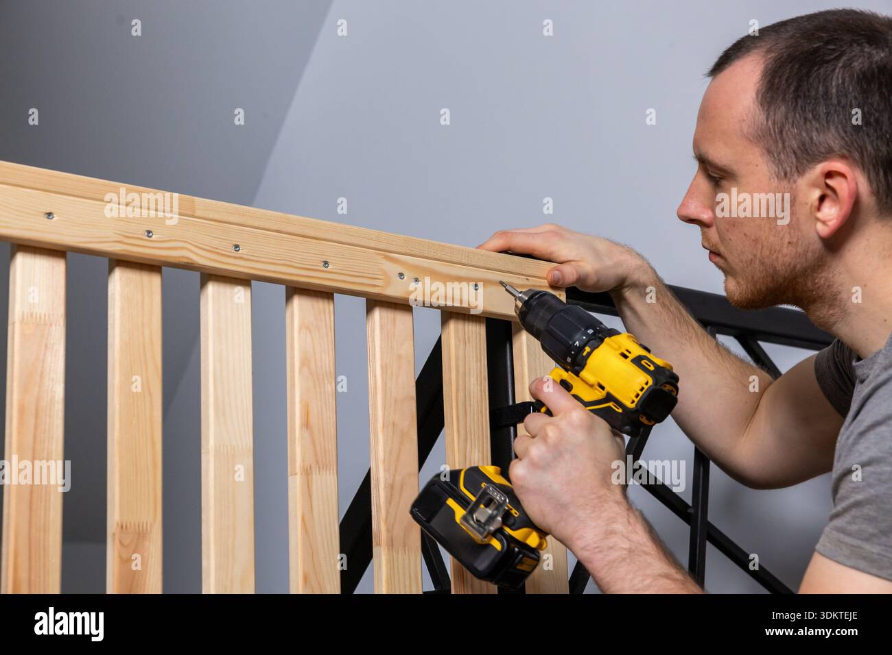 A man secures screws into a wooden railing with a yellow and black ...