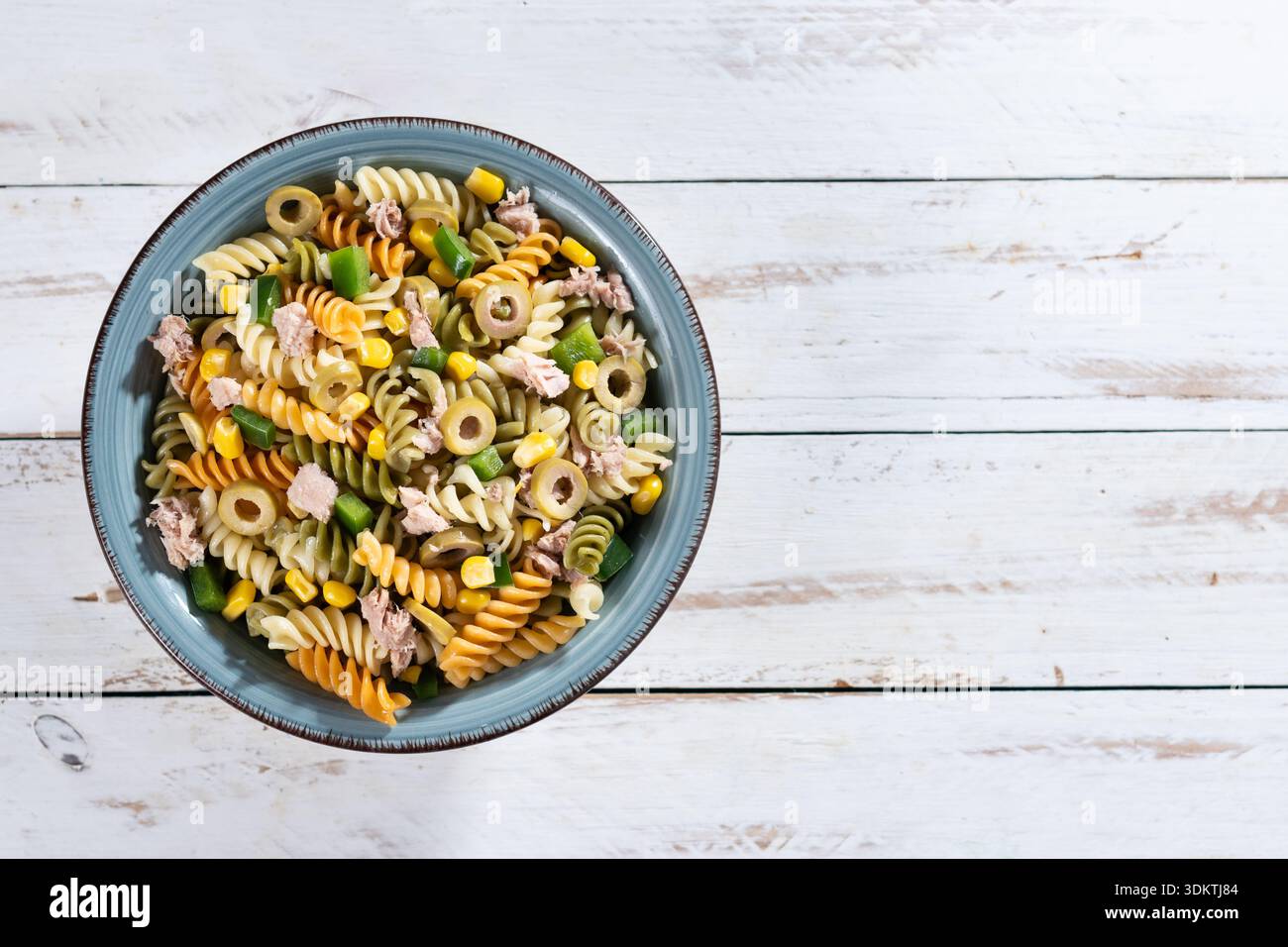 Pasta salad with tuna, corn and olives in bowl on wooden table Stock Photo