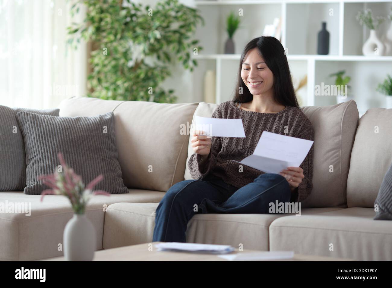 Happy asian woman reading letter sitting on a couch at home Stock Photo