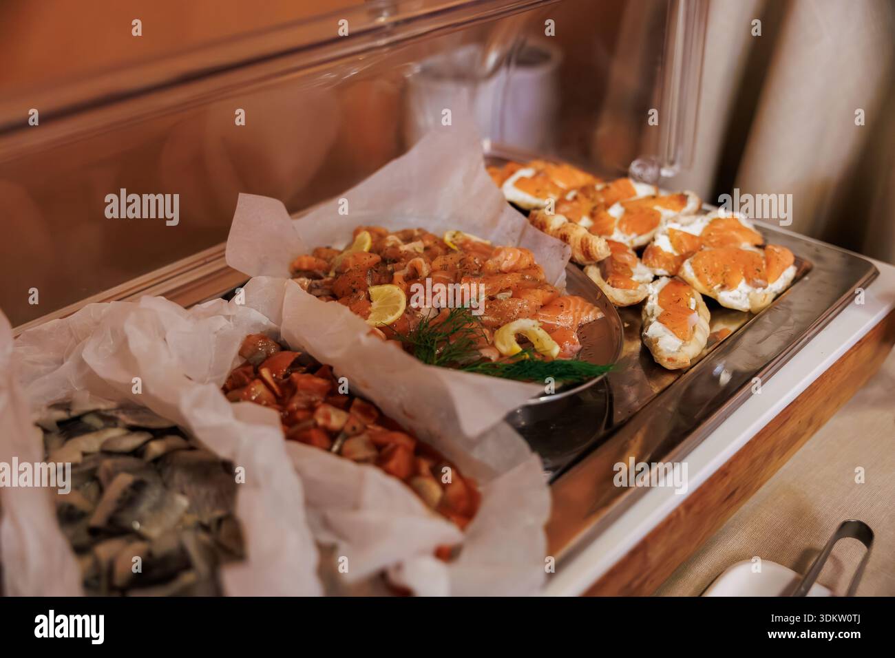 Caterers present cold dishes at an indoor Scandinavian buffet. Salmon gravlax with lemon and dill, marinated fish, pickled herring, and canapes sit in Stock Photo
