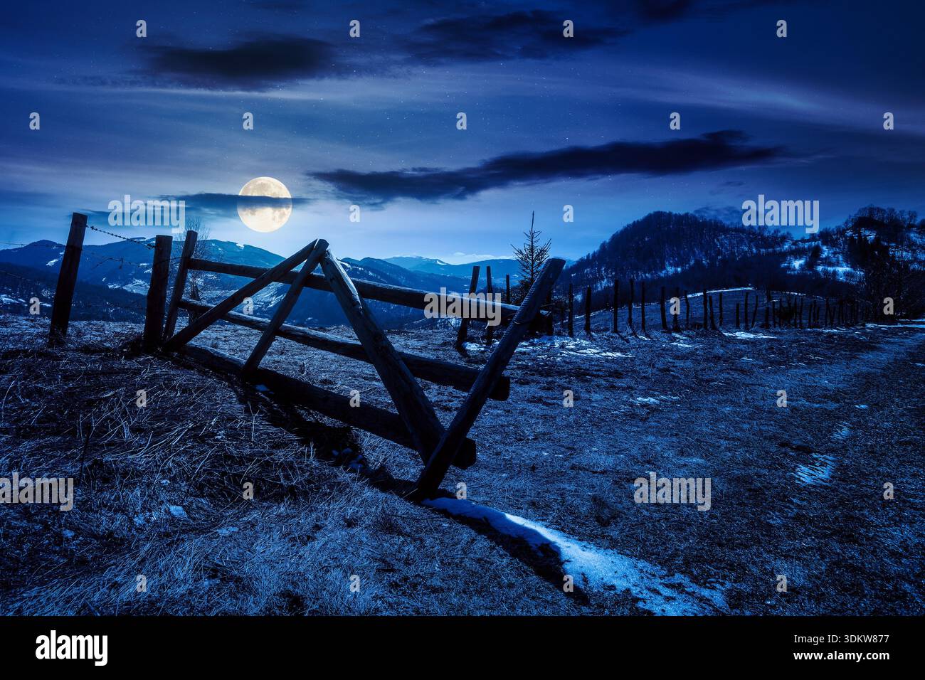 rural landscape of carpathian mountains in early spring under dark sky at night. snow covered hill with barbed wire fence in full moon light. inner st Stock Photo