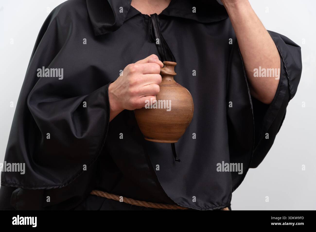 Hands of monk in black robe holding clay jug isolated on white background studio Stock Photo