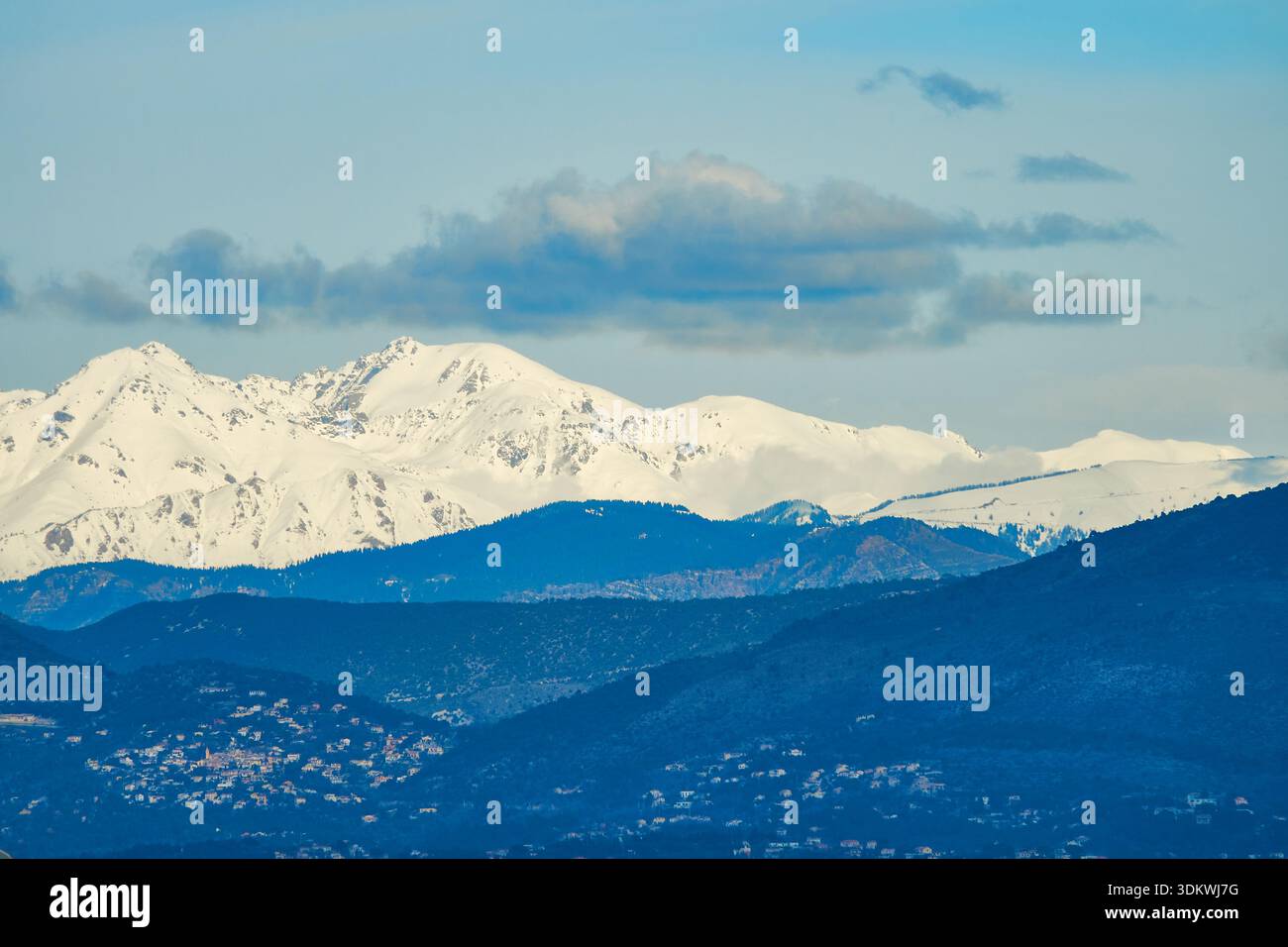 Snow-Capped Mountain Range Under Clear Blue Sky With Clouds and Rolling Foregrounds Stock Photo