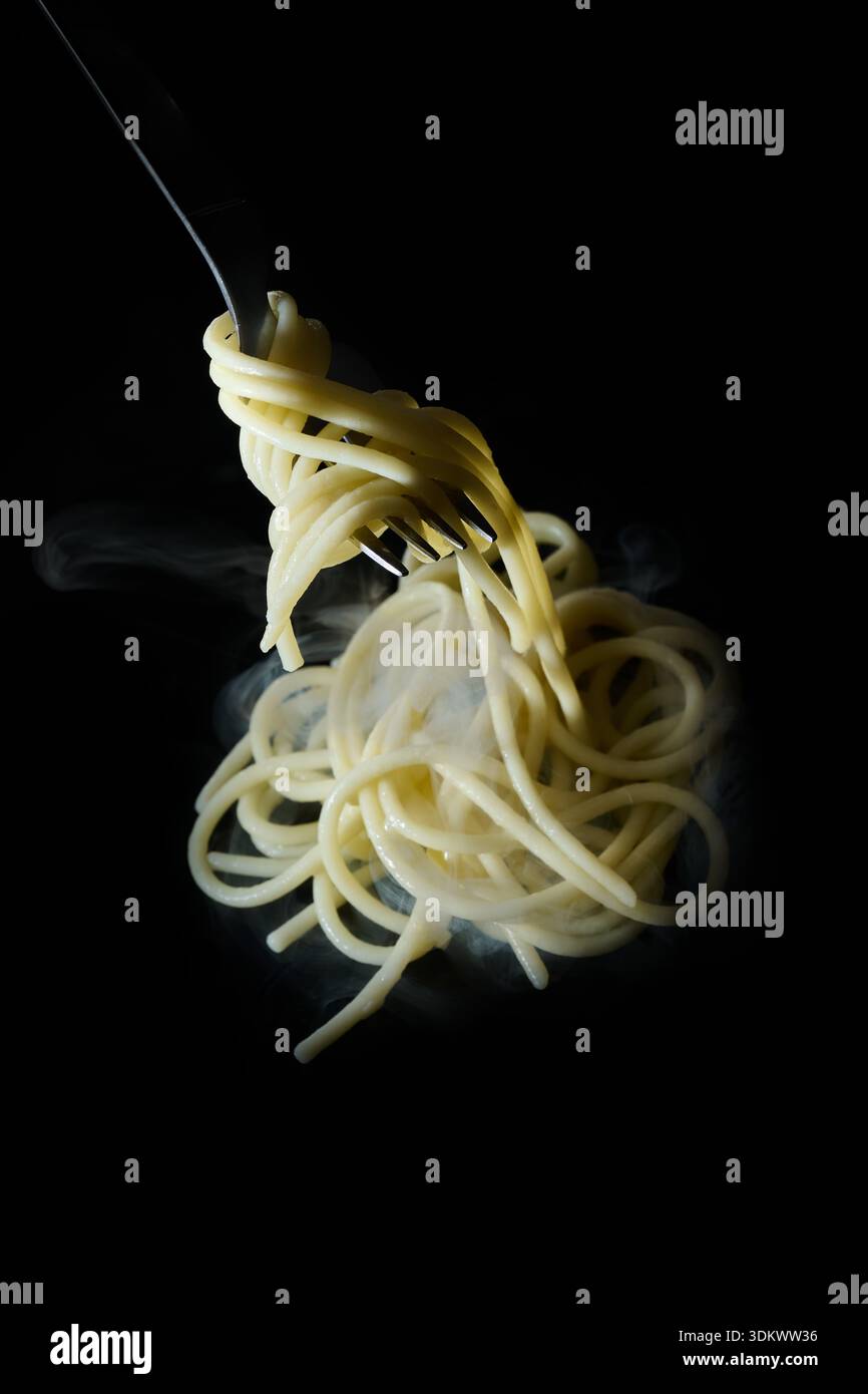 Steaming hot spaghetti swirling on a fork against a dark background, representing delicious italian pasta cuisine Stock Photo
