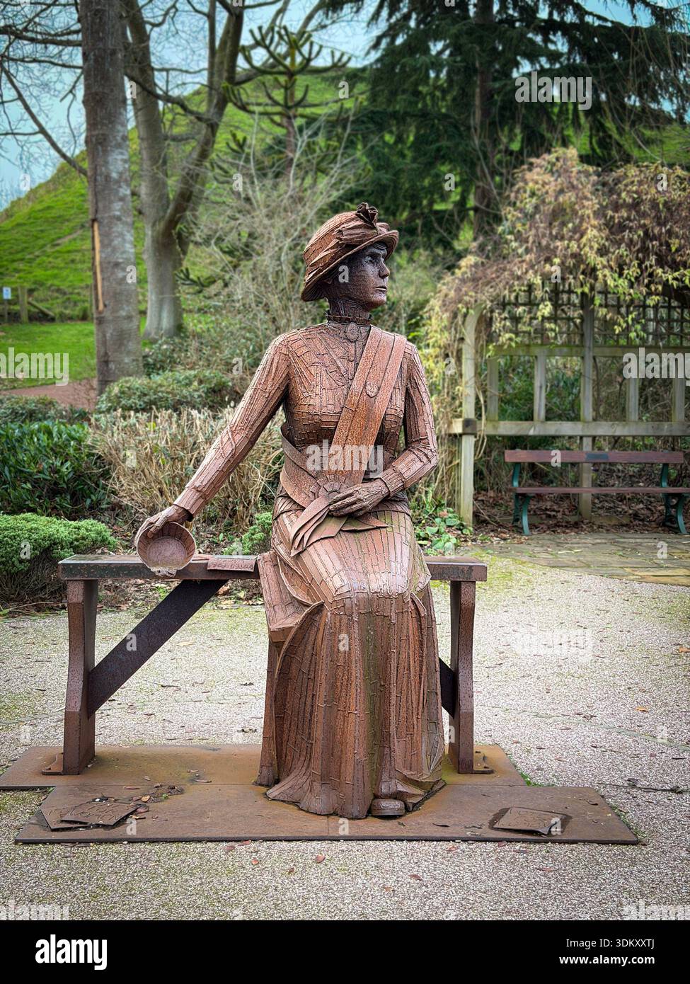 A rusty corten steel statue of militant suffragette Emily Wilding Davison by sculptor Ray Lonsdale seated on a bench in Carlisle Park,Morpeth, - Smartphone Captured Stock Image