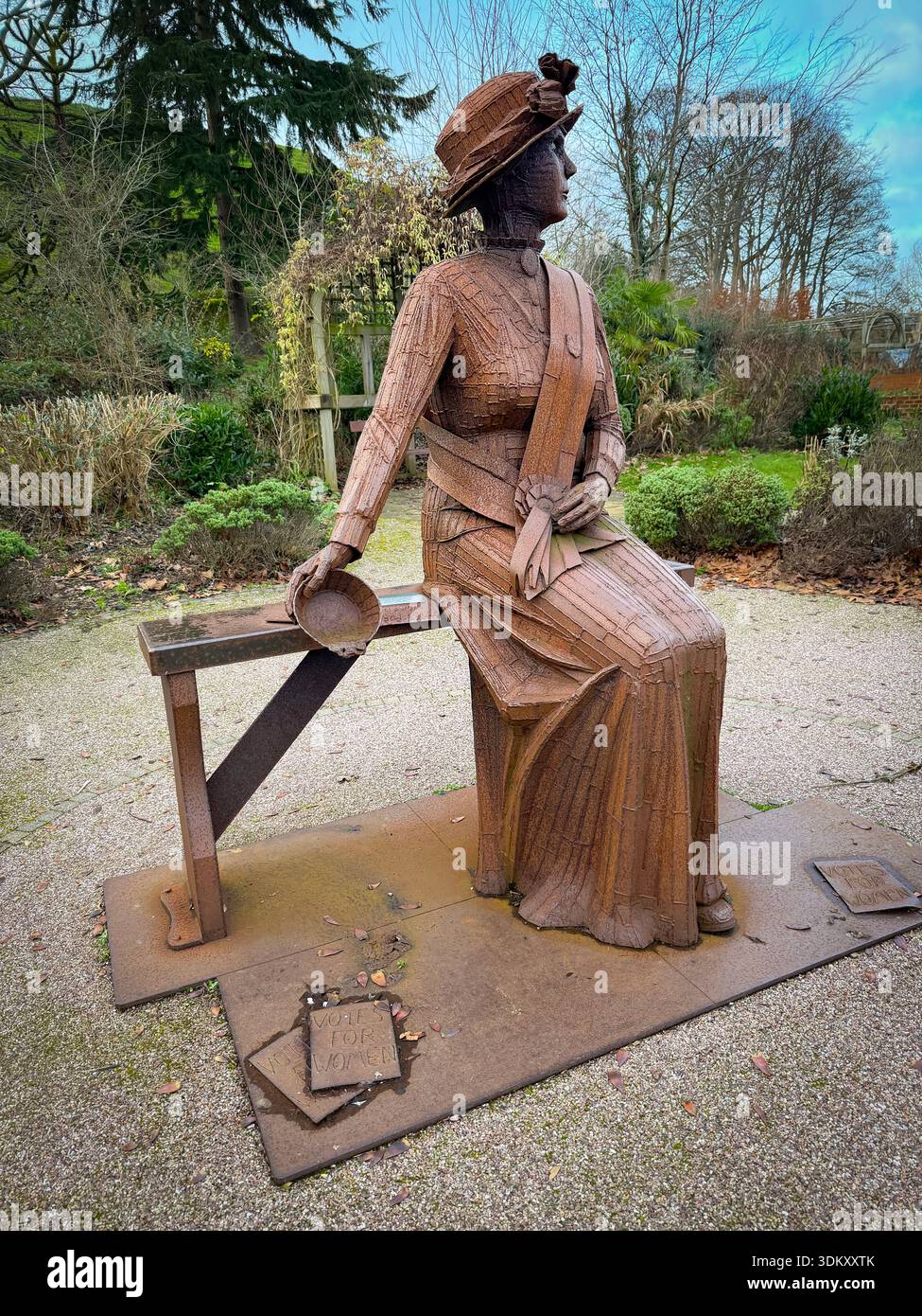 A rusty corten steel statue of militant suffragette Emily Wilding Davison by sculptor Ray Lonsdale seated on a bench in Carlisle Park,Morpeth, - Smartphone Captured Stock Image