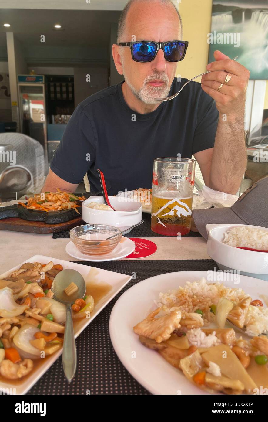 A middle aged man enjoying a meal at an asian  casual dining restaurant, surrounded by flavorful dishes and a cold drink - Smartphone Captured Stock Image
