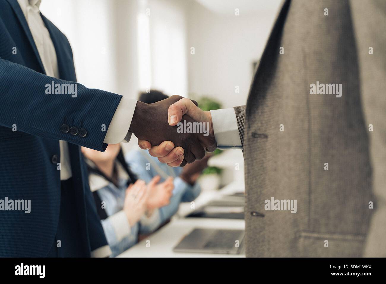 A diverse pair of business professionals shake hands in a bright office ...