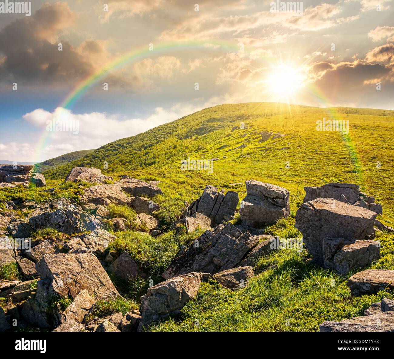 sunny mountain landscape in summer under blue sky at sunset. lush green grass and sharp rocks on steep hillside in evening light. beautiful view of re Stock Photo