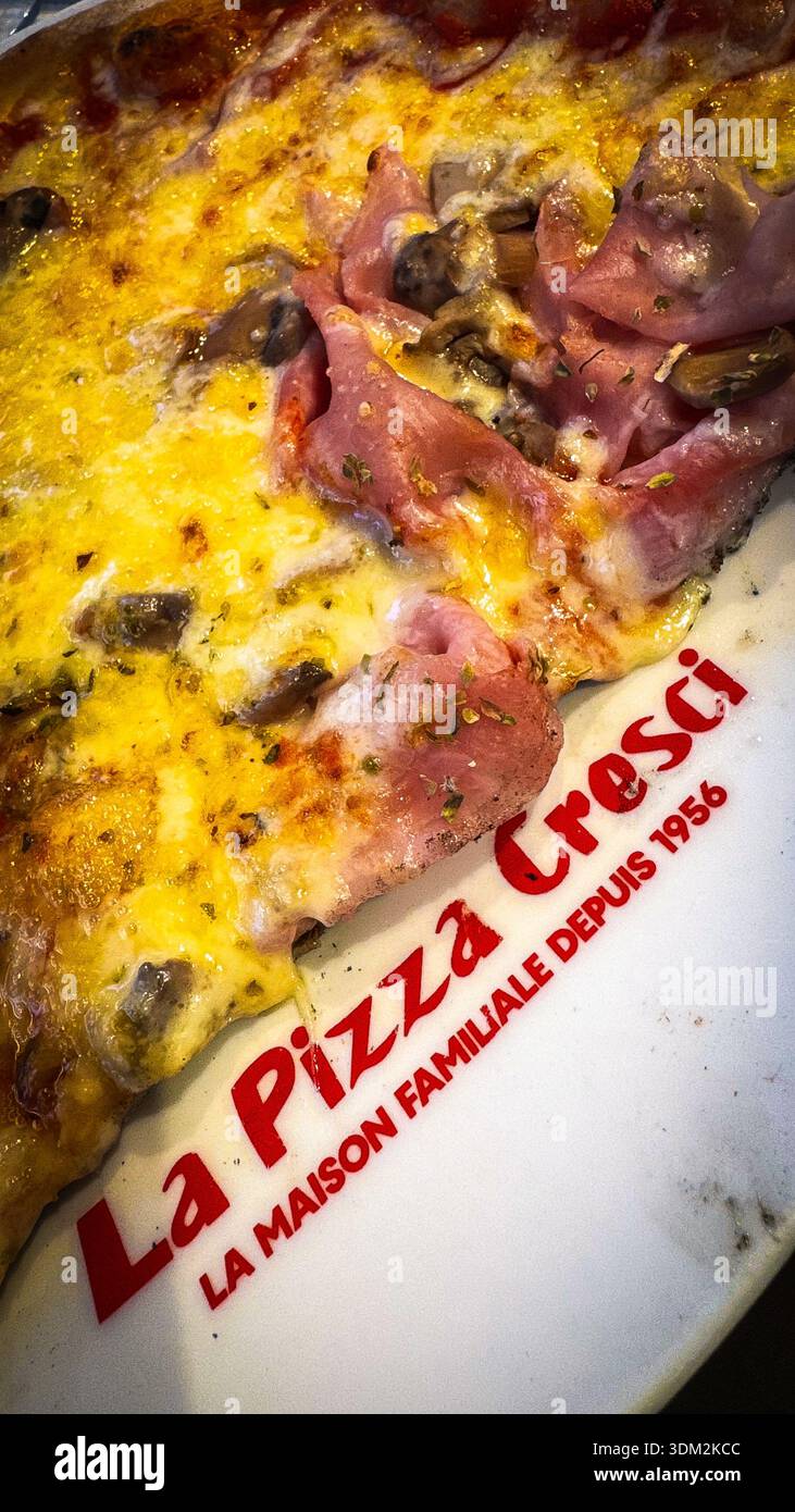 Close-up slice of ham and mushroom pizza with melted golden cheese on thin crust from La Maison Familiale Creci pizzeria, served on white plate - Smartphone Captured Stock Image
