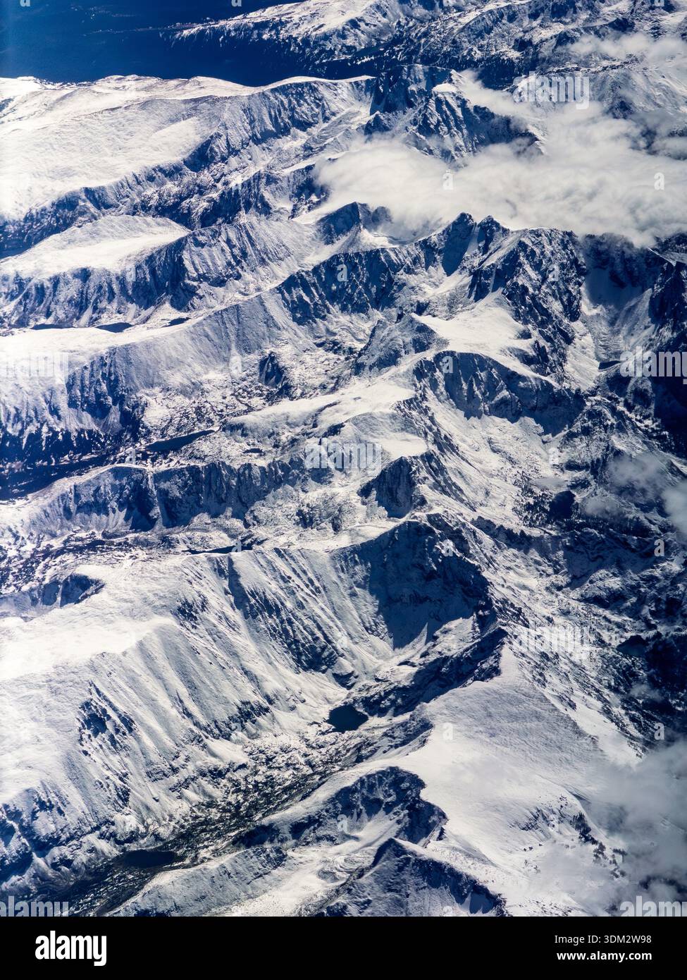 Aerial plane window view of vast Rocky Mountains with snow-covered ridges, peaks and blue waters below - Smartphone Captured Stock Image