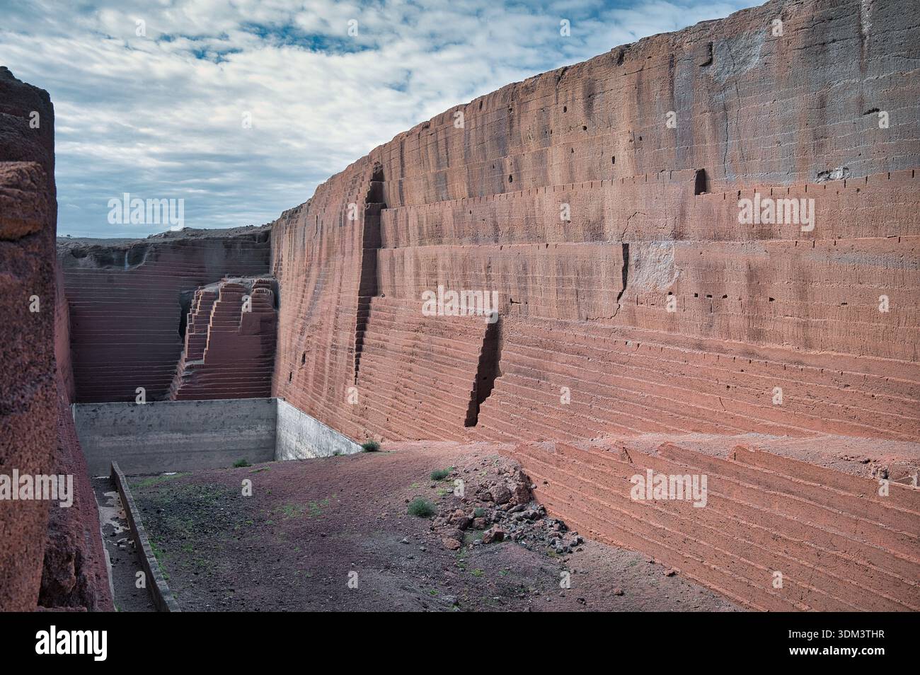 Wide-angle view of an abandoned volcanic quarry carved into layered red and brown rock formations in Lanzarote, Canary Islands. Stock Photo