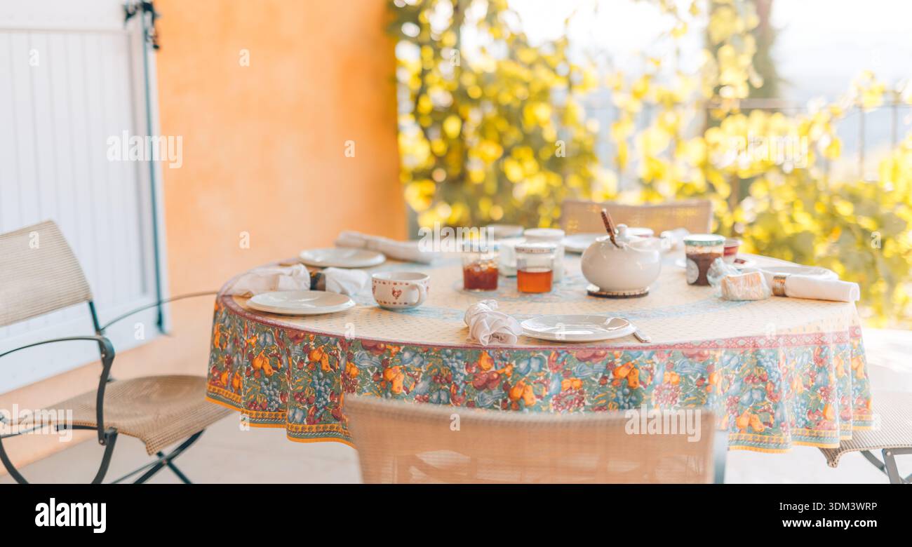 Morning cozy breakfast table in Mediterranean countryside, idyllic relaxing mood, blurred foliage, peaceful outdoor landscape Stock Photo