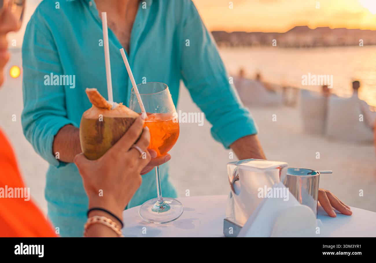 Couple cheering with cocktails sunset ocean beach view vibrant optimism cloud dancer color trend 2026 slow travel romantic mood Stock Photo