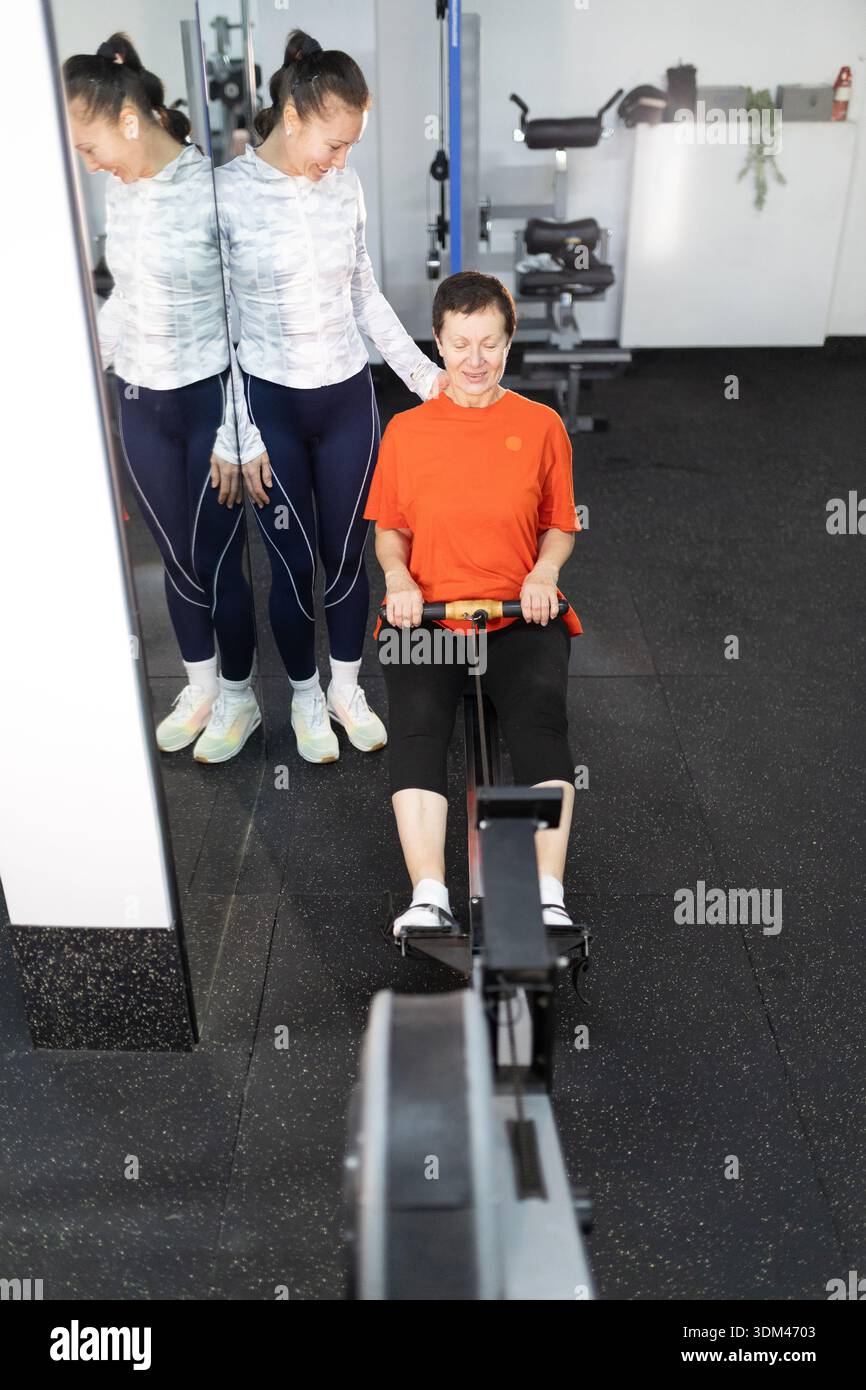 Personal trainer guiding senior woman on rowing machine Stock Photo - Alamy