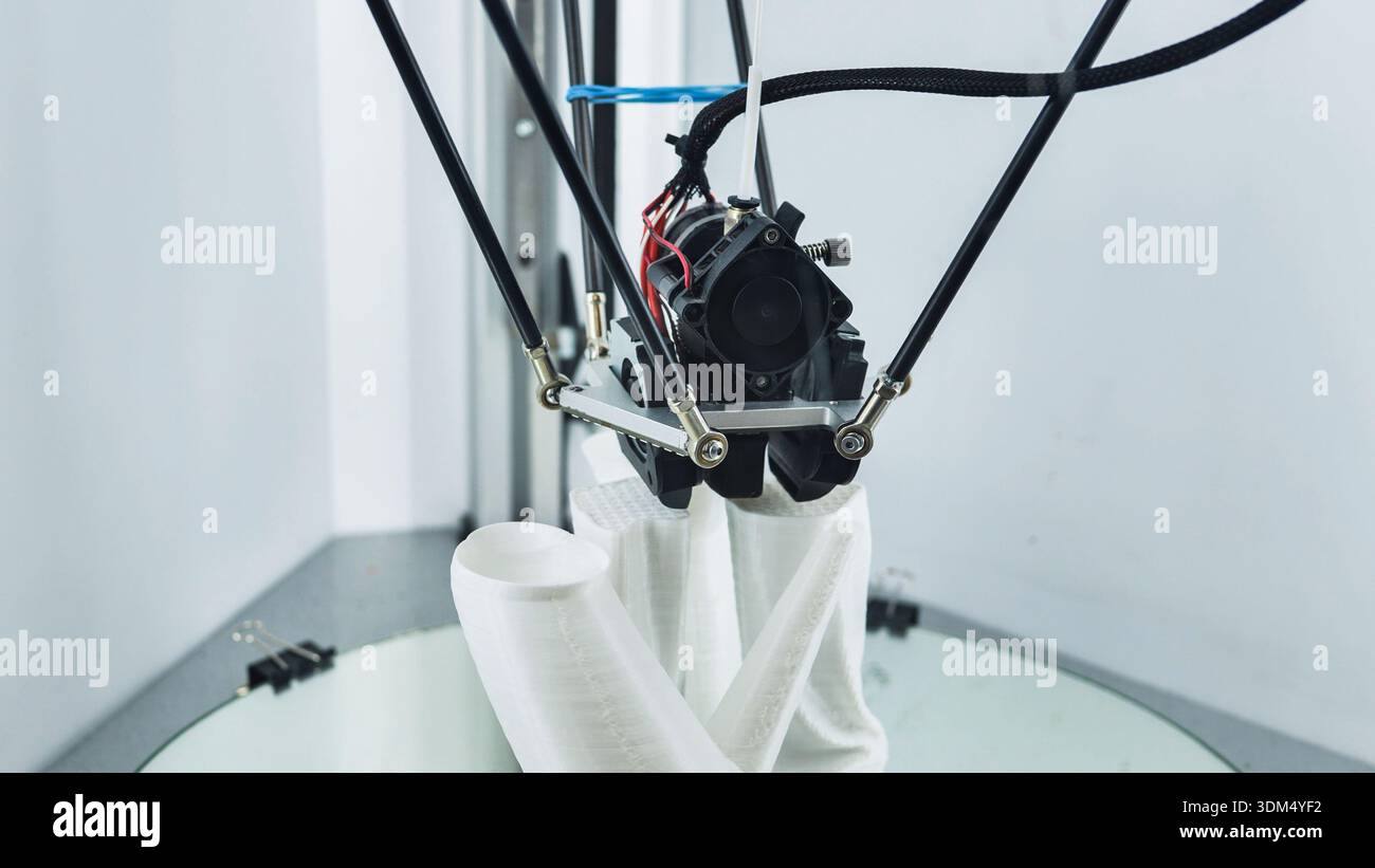 3D printer nozzle creating a white prototype object on a build plate Stock Photo
