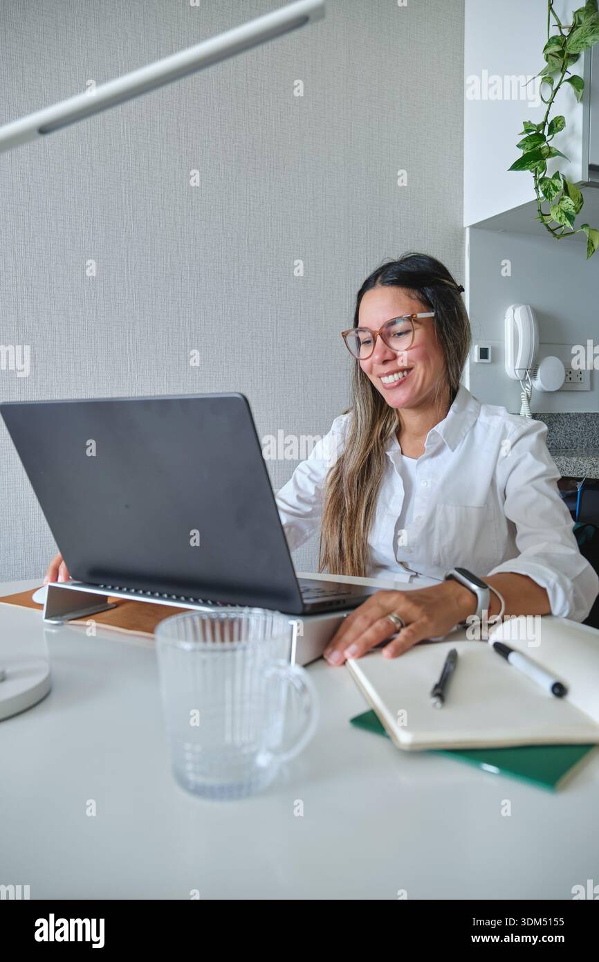 Smiling woman sitting at desk using laptop for remote work Stock Photo