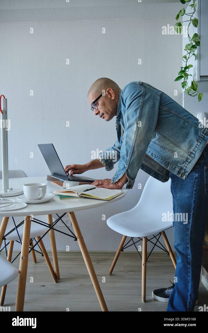 Man using laptop and notebook while leaning during remote work Stock Photo