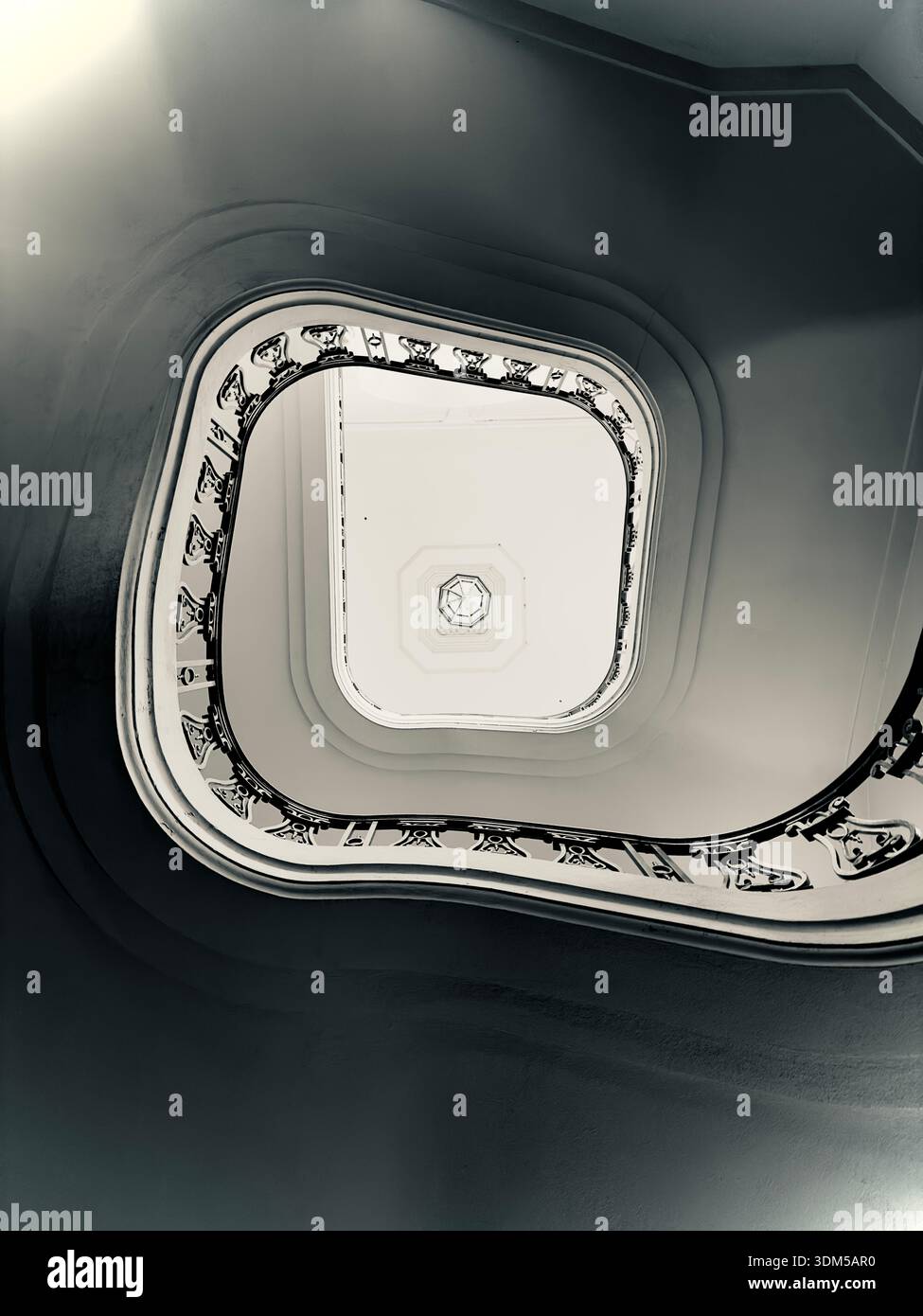 Abstract black and white view looking up through a curved stairwell with ornate railings and strong architectural symmetry - Smartphone Captured Stock Image