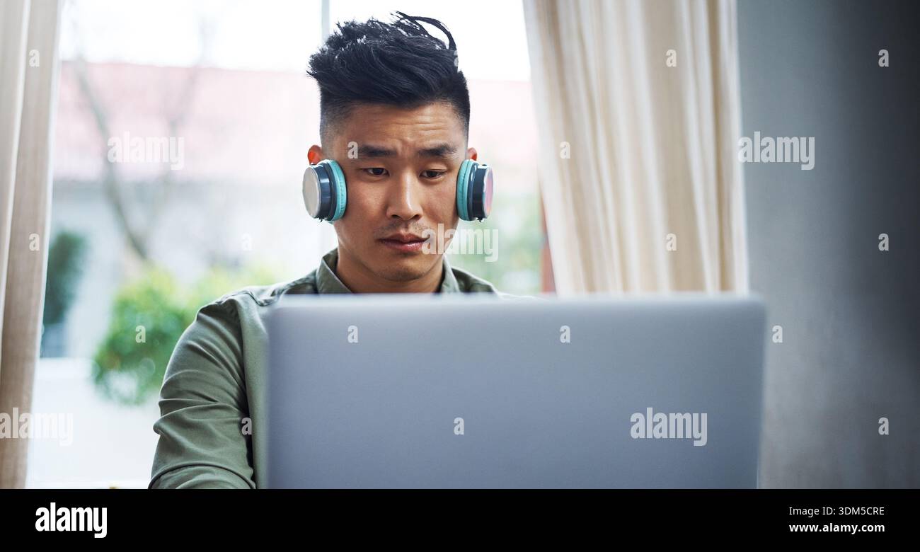 Headphones, programming or asian man with laptop for remote work, system maintenance or development. Tech, freelancer or developer in home for Stock Photo