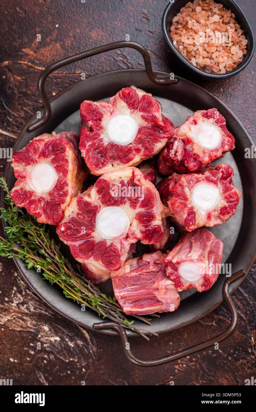Raw Oxtail pieces in pan with fresh thyme, top view rustic food scene showing collagen rich beef for stock. Stock Photo