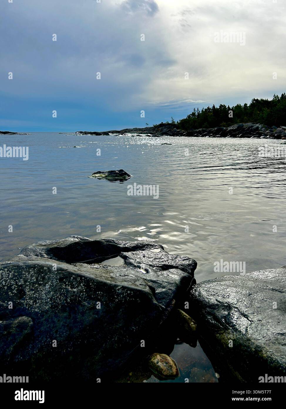 Dramatic sky over calm Baltic Sea with rocky pine-covered headland along the Swedish coastline Stock Photo