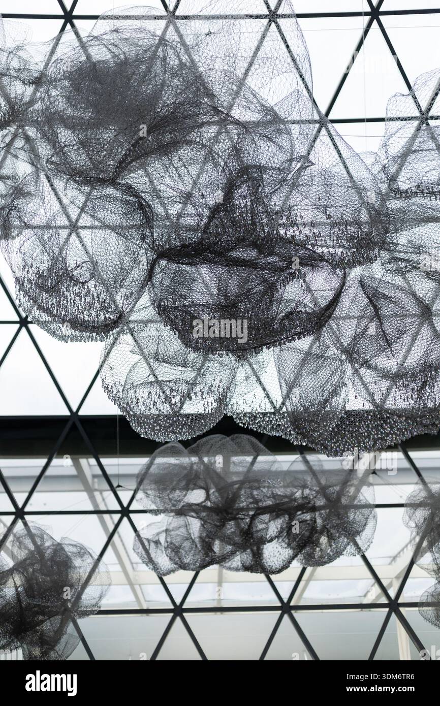 Large black mesh structures float under a geometric ceiling in an airy space. Light filters in, creating an engaging and visually interesting atmosphe Stock Photo