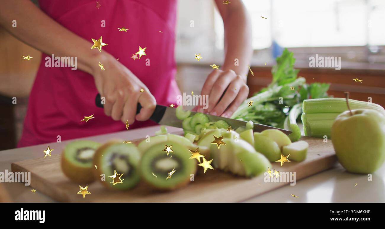 Slicing woman in bright pink top using black-handled knife on kitchen countertop, with kiwis Stock Photo