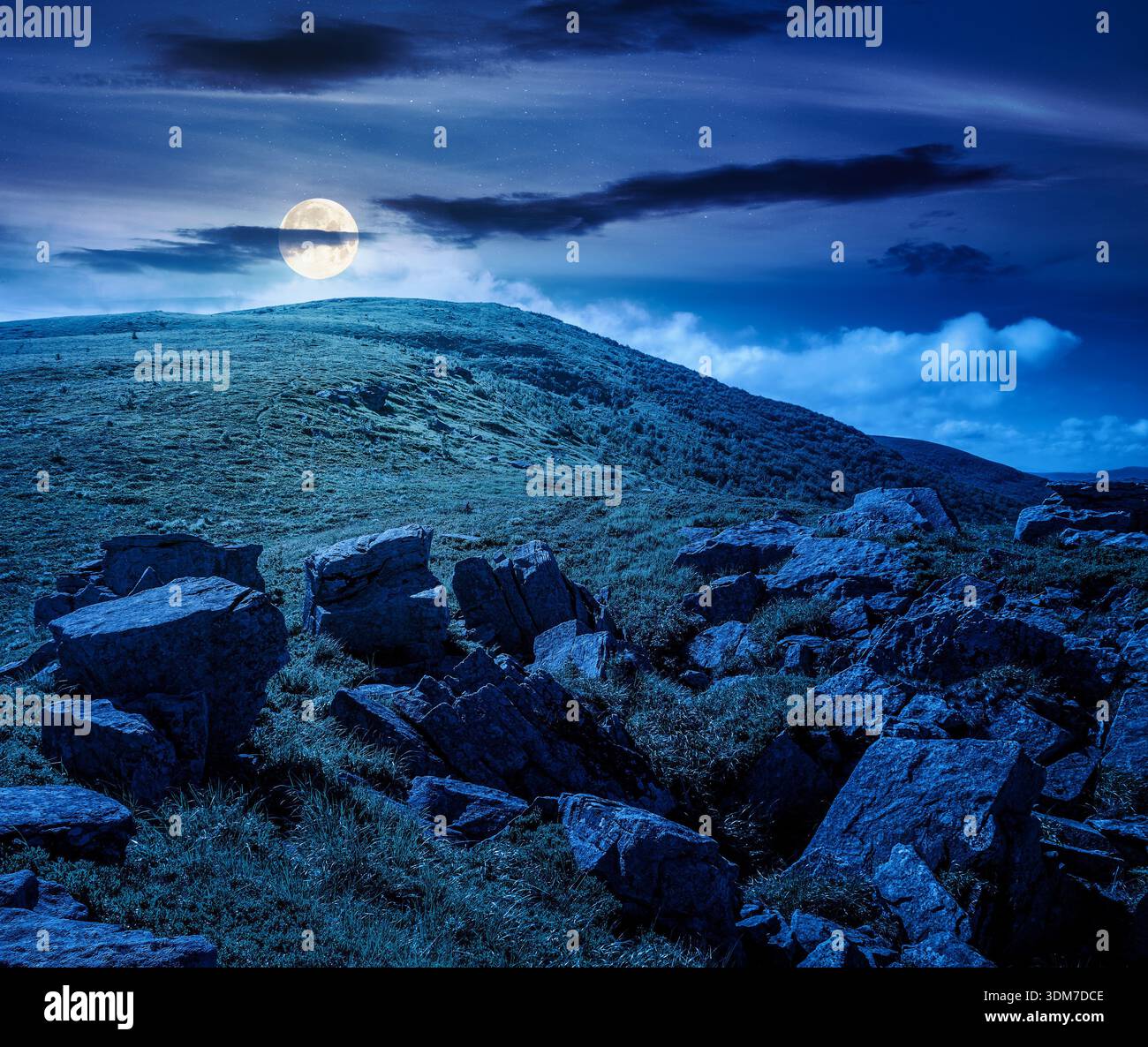 mountain landscape in summer under dark sky at night. lush green grass and sharp rocks on steep hillside in full moon light. beautiful view of remote Stock Photo