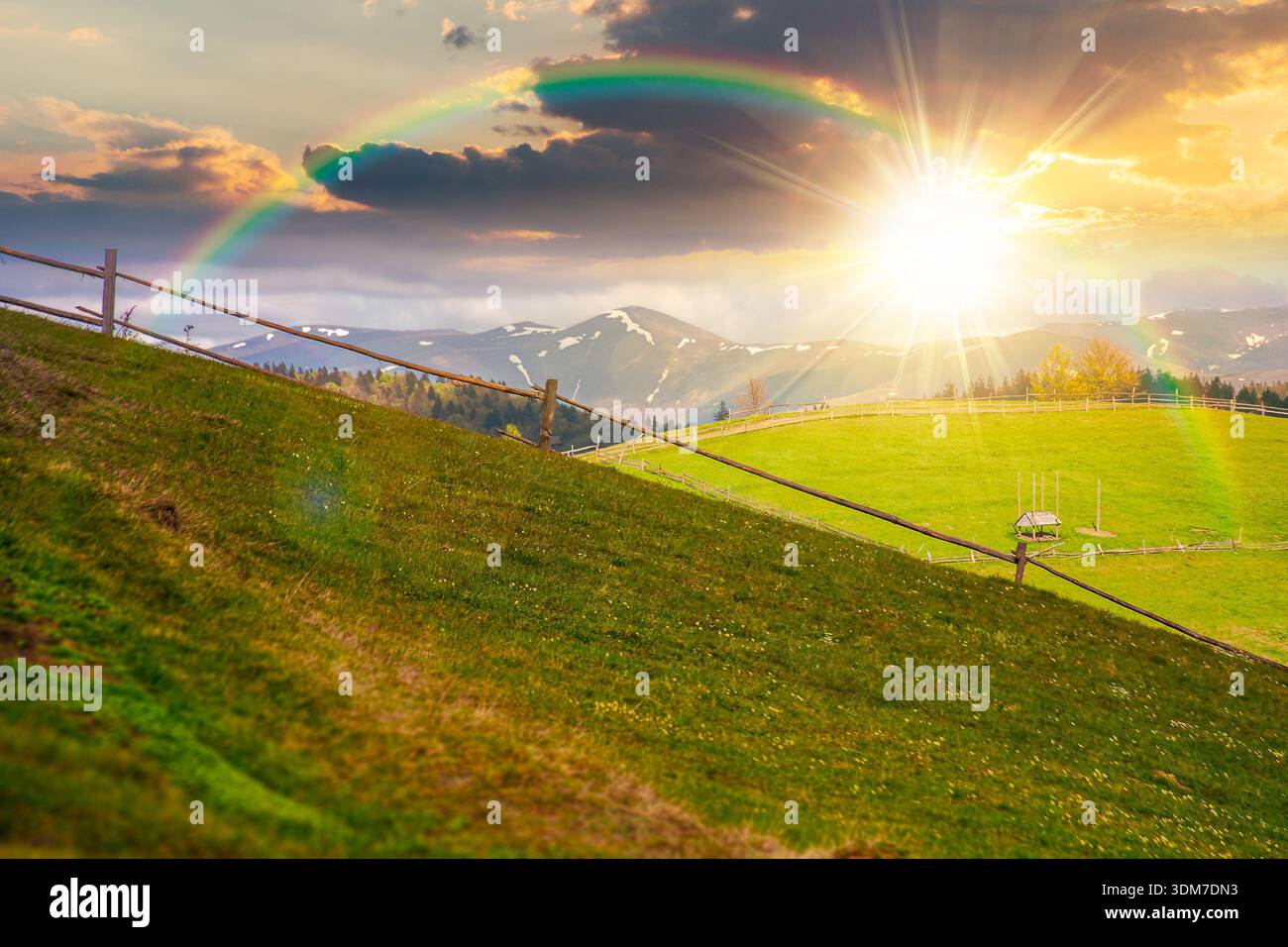 green rural landscape with wooden fence at sunset. countryside scene with rolling hill in spring in evening light. pastoral highland region on cloudy Stock Photo