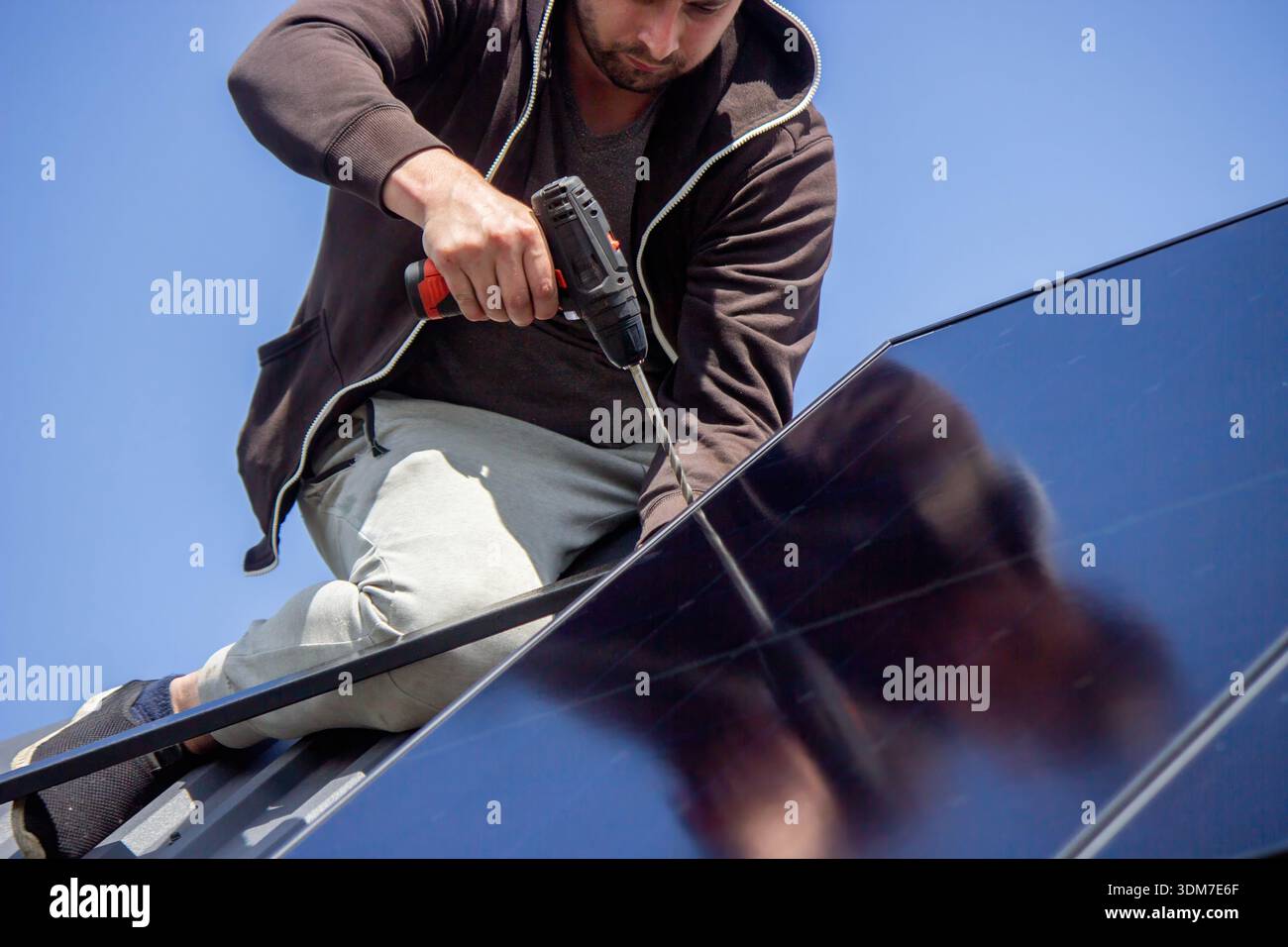 Installer fixing solar panel with a cordless drill on a residential house roof Stock Photo