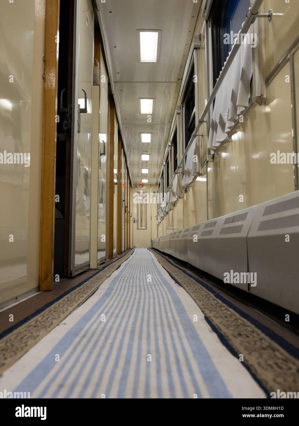 Train journey corridor presenting empty pathway with blue striped runner carpet Stock Photo