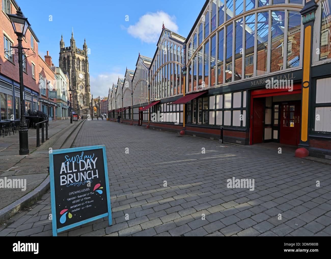 Stockport Market Place with the Victorian Market Hall frontage and an “All Day Brunch” pavement sign in winter sunshine, with St Mary’s Church tower Stock Photo