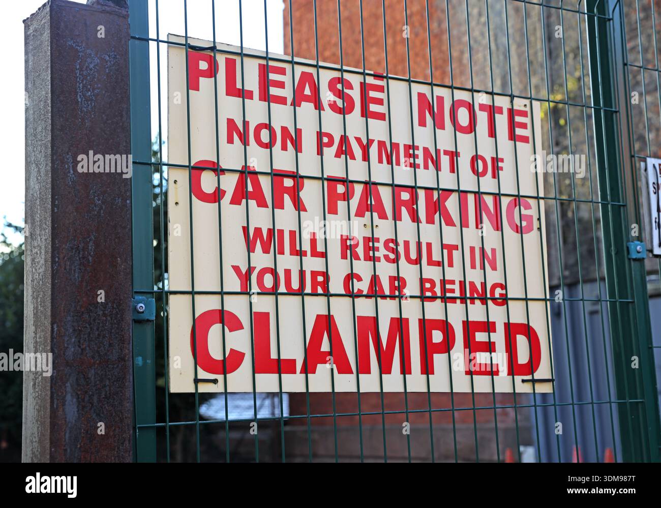 Close-up of a private car park warning sign behind a metal fence stating “Non payment of car parking will result in your car being clamped”, Stockport Stock Photo