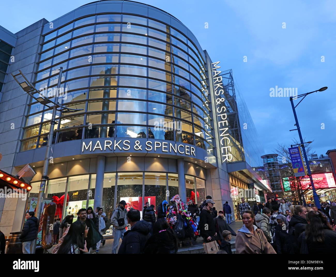 Marks & Spencer department store Market Street in Manchester city centre at winter dusk, with crowds of shoppers outside the illuminated curved glass Stock Photo