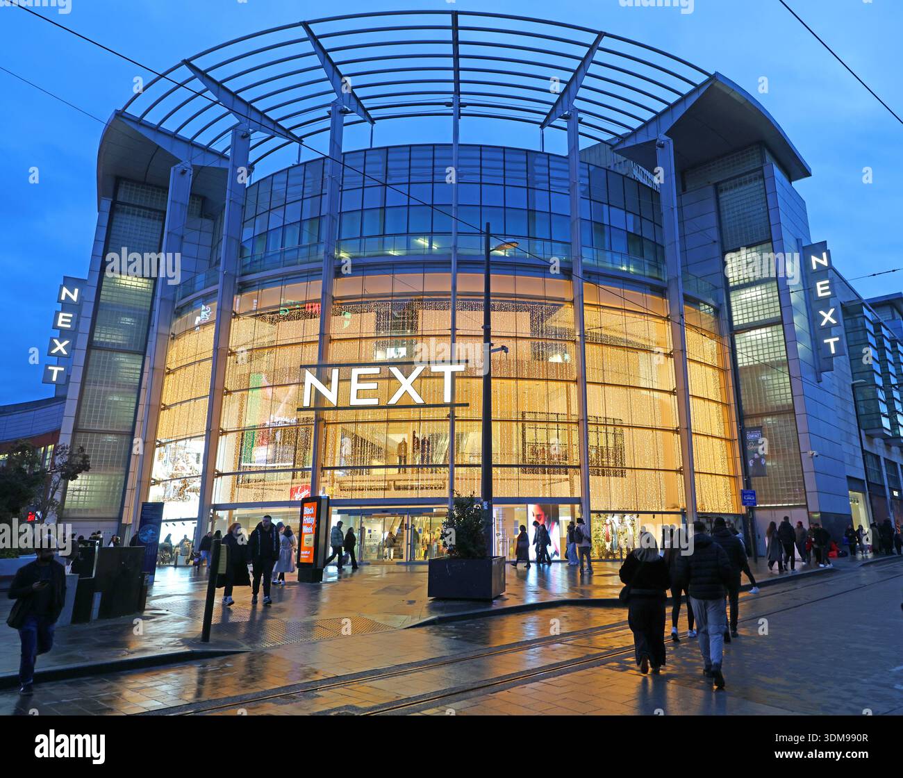 Illuminated NEXT department store at dusk in winter, outside Manchester Arndale by Exchange Square, Manchester city centre, England, UK, with shoppers Stock Photo