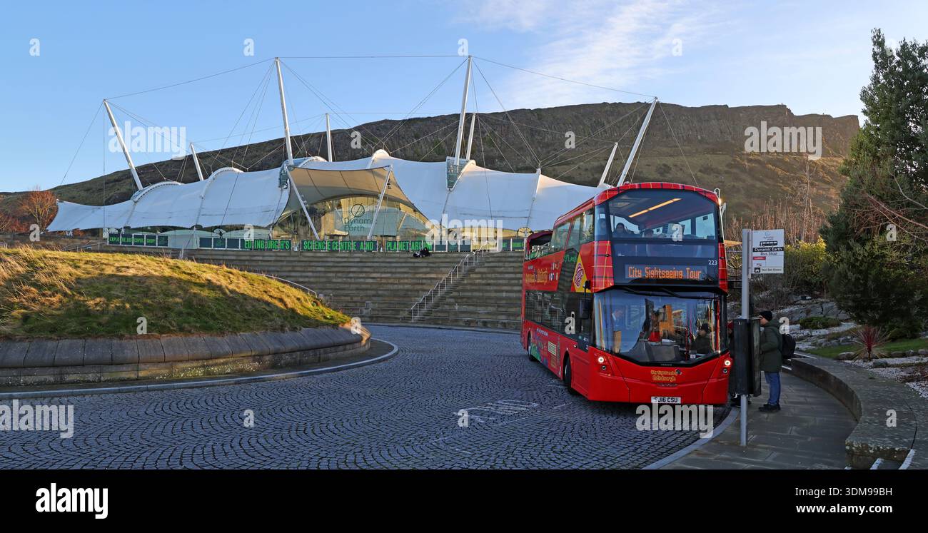 Red open-top sightseeing tour bus outside Dynamic Earth science centre and planetarium on Holyrood Road, with Salisbury Crags and Holyrood Park winter Stock Photo