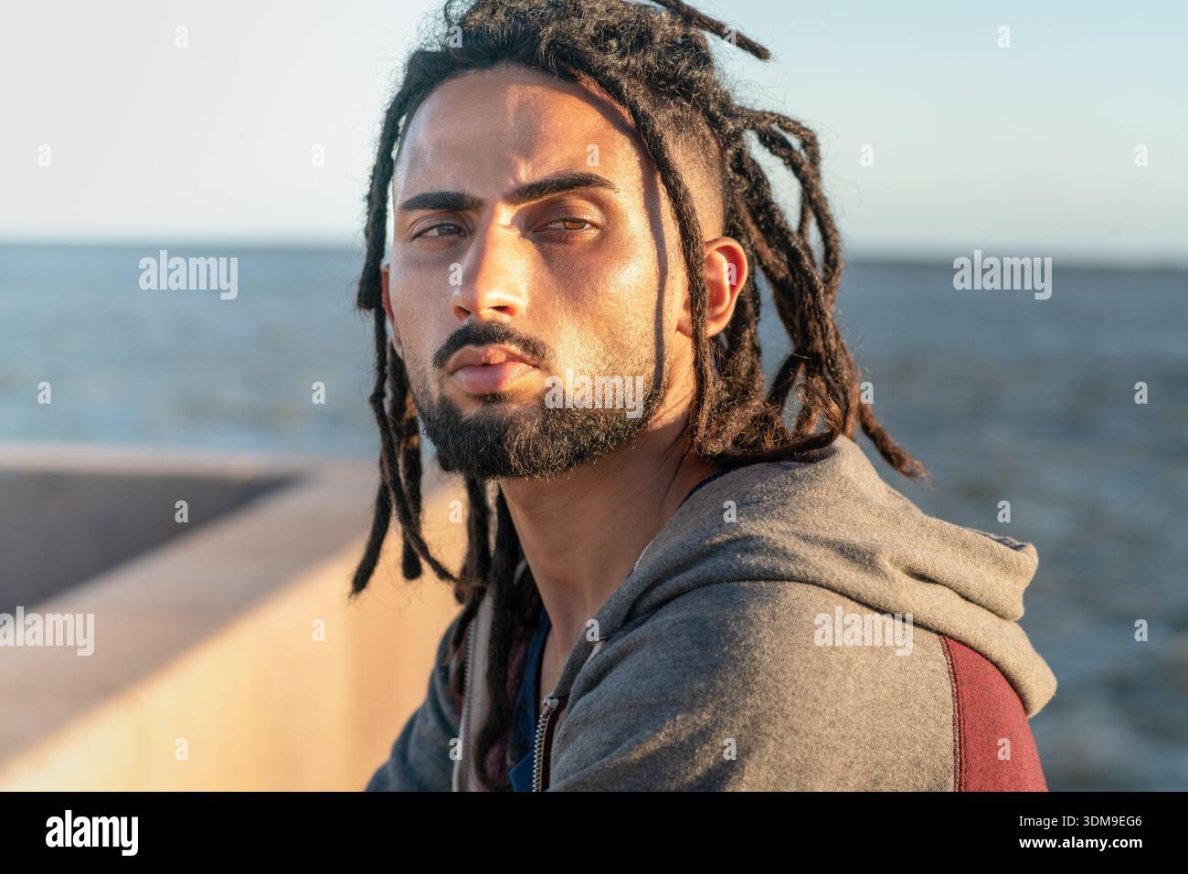 Young man with dreadlocks and beard standing outdoors by the sea Stock Photo