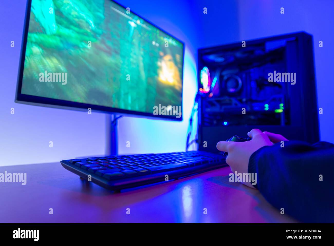 Gamer holding game controller while playing video game on computer monitor at modern gaming desk with illuminated desktop pc Stock Photo