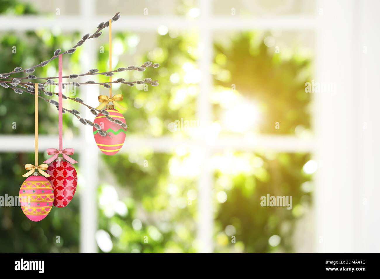 Easter eggs hanging from willow branches near window indoors Stock Photo