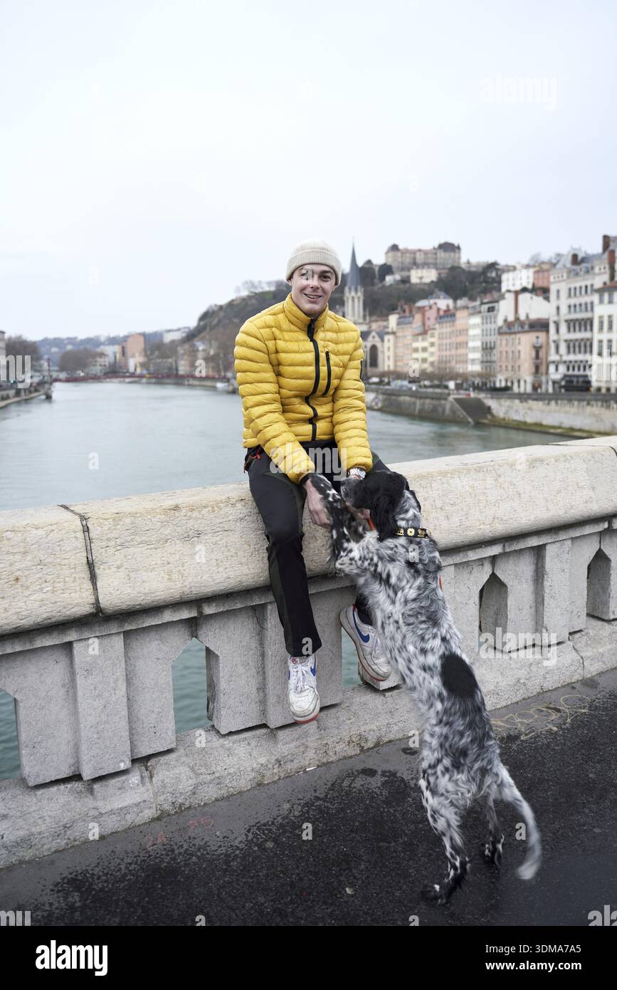 Luring and attracting a dog, dogownership, dog training, going walkies in city, person in a yellow jacket sits on a bridge as a dog jumps up to reach Stock Photo