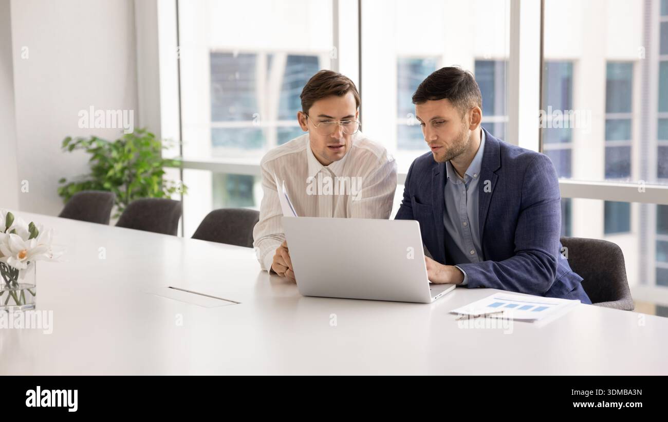 Two focused men working together on presentation using laptop Stock Photo