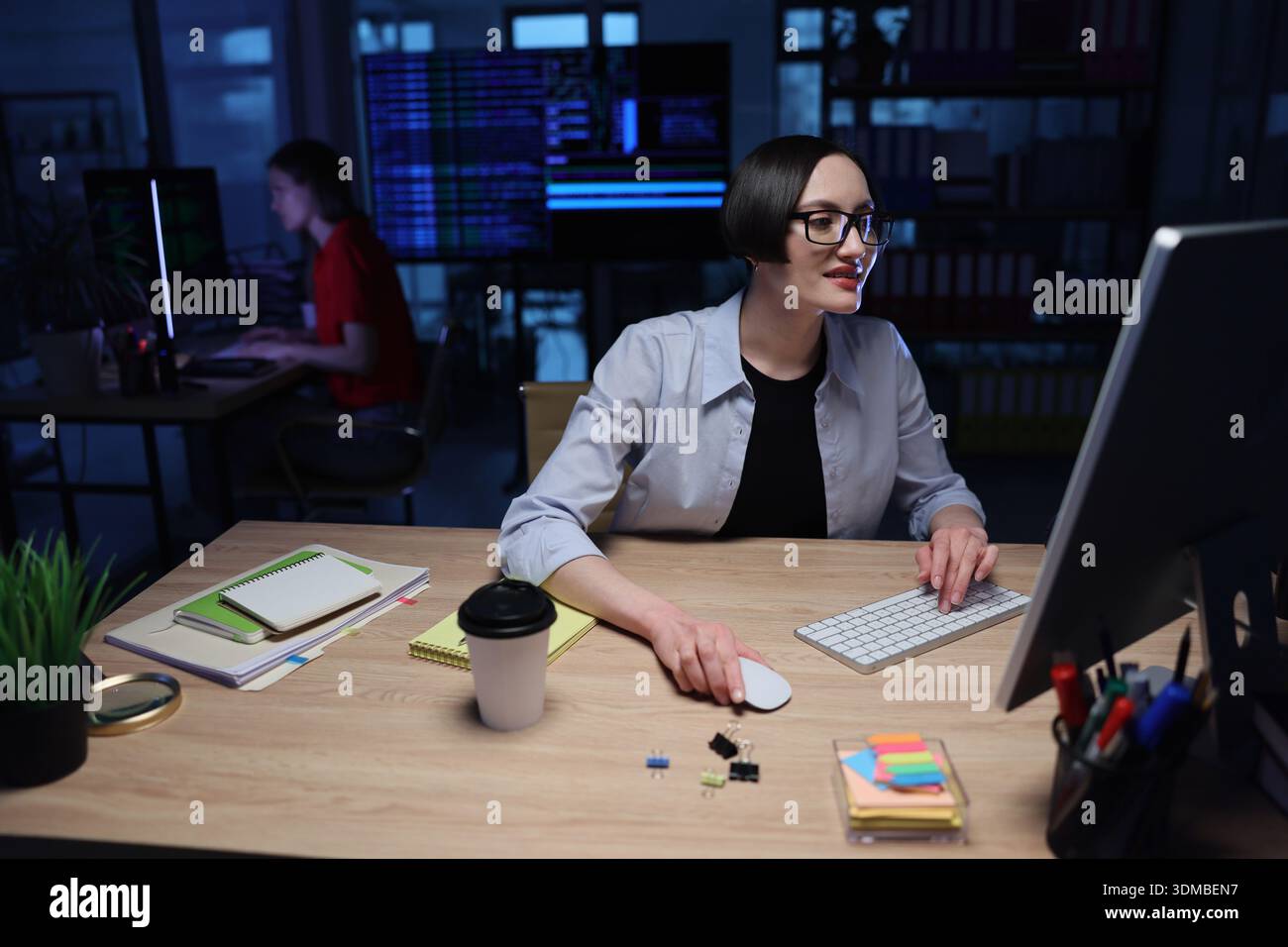 Creative coding session in a modern workspace during nighttime with focused individuals working on computers Stock Photo