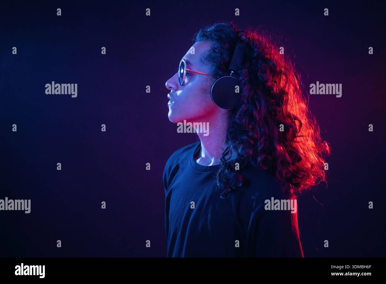 Long hair, headphones, side view. Guy is indoors at night with neon lighting. Stock Photo